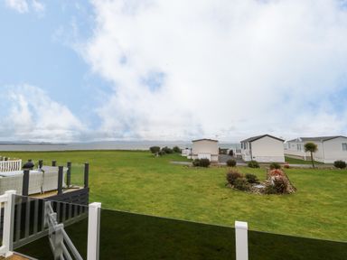 A grassy area with small mobile homes near a body of water and a deck with outdoor furniture at Seafront Holiday Home 2 in Pwllheli