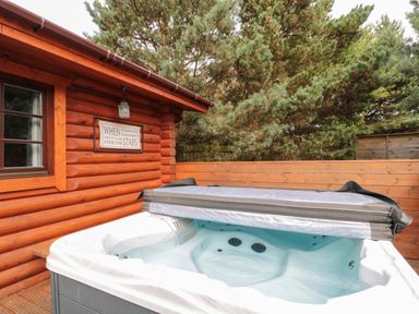 An outdoor hot tub next to a wooden log cabin with a framed sign on the wall at Welcome Hjem Log Cabin Morpeth near Felton