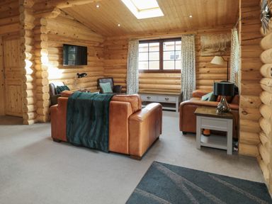 A living room with leather sofas armchairs a TV and a side table at Welcome Hjem Log Cabin Morpeth near Felton