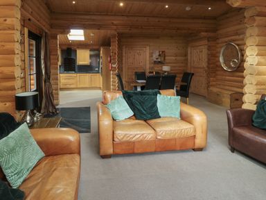 A log cabin living room with leather sofas green cushions and a dining table with black chairs at Welcome Hjem Log Cabin Morpeth near Felton