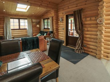 A living area with a dining table and chairs a sofa and windows in a log cabin Welcome Hjem Log Cabin Morpeth near Felton