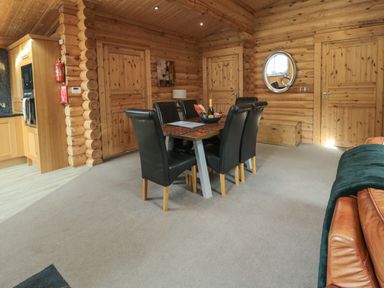A dining area with a table and six chairs inside a wooden log cabin with doors and a round mirror on the wall at Welcome Hjem Log Cabin in Morpeth near Felton