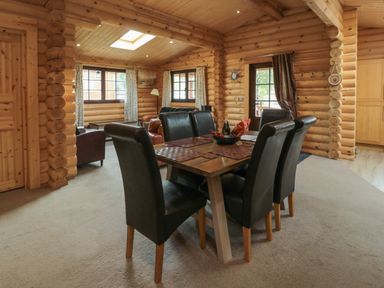 A dining area with a wooden table and six black chairs in a log cabin with windows and a door at Welcome Hjem Log Cabin Morpeth near Felton