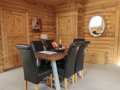 A dining area with a rectangular table surrounded by six black chairs and wooden doors and walls at Welcome Hjem Log Cabin Morpeth near Felton
