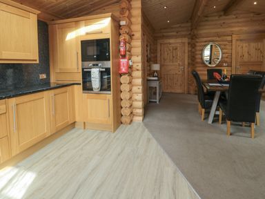 A kitchen with wooden cabinets next to a dining area with a table and black chairs at Welcome Hjem Log Cabin in Morpeth near Felton