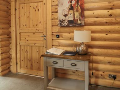 A wooden door next to a table with a lamp and books in a log cabin wall room at Welcome Hjem Log Cabin Morpeth near Felton