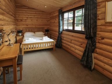 A bedroom with a double bed bedside tables desk lamp and window with curtains at Welcome Hjem Log Cabin in Morpeth near Felton