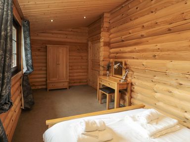A bedroom with a bed and towels a wooden wardrobe and a desk with a lamp and mirror at Welcome Hjem Log Cabin Morpeth near Felton