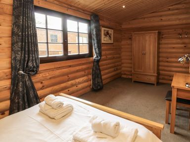 A bedroom with a bed and folded towels by a window with curtains a wooden wardrobe and a desk at Welcome Hjem Log Cabin Morpeth near Felton