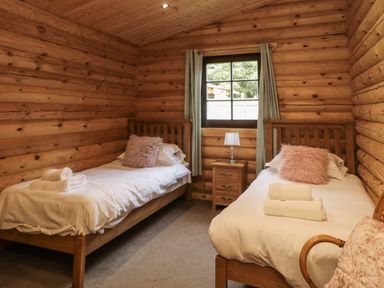 A bedroom with two single beds a nightstand with a lamp and a window at Welcome Hjem Log Cabin Morpeth near Felton
