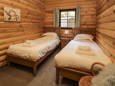 A bedroom with two single beds a bedside table with a lamp and a window at Welcome Hjem Log Cabin Morpeth near Felton