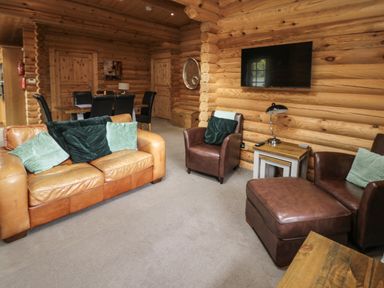 A living room with leather sofas and armchairs a TV on the wall and a dining table with chairs in the background at Welcome Hjem Log Cabin Morpeth near Felton