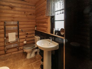 A bathroom with a toilet sink towel rack and window at Welcome Hjem Log Cabin in Morpeth near Felton