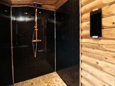 A shower area with black glittery wall panels wooden log walls and a square overhead shower at Welcome Hjem Log Cabin Morpeth near Felton