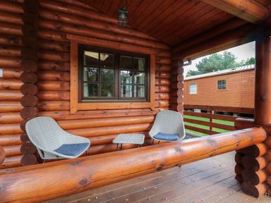 A porch with two chairs and a small table at Welcome Hjem Log Cabin in Morpeth near Felton