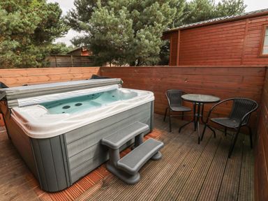 An outdoor deck with a hot tub a small round table and two chairs at Welcome Hjem Log Cabin Morpeth near Felton