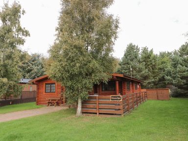 A log cabin with a fenced porch surrounded by trees and grass at Welcome Hjem Log Cabin in Morpeth near Felton