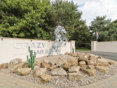 An outdoor area with a metal horse sculpture surrounded by rocks in front of a wall with the sign Crazy Horse Bar and Grill at Welcome Hjem Log Cabin Morpeth near Felton