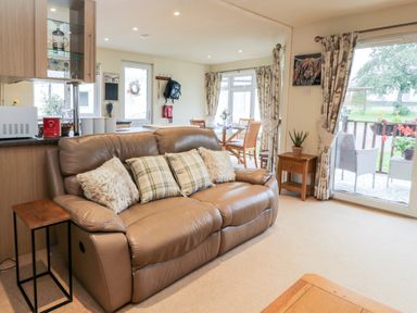 A living room with a leather sofa and pillows near a sliding glass door and dining area at Eden Lodge Castlewigg near Whithorn