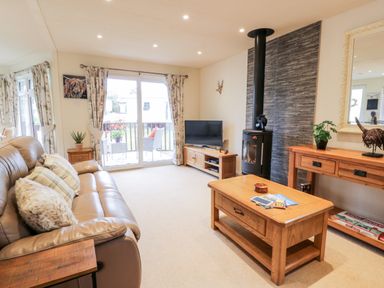 A living room with a brown leather sofa wooden coffee table wooden TV cabinet and a wood stove at Eden Lodge in Castlewigg near Whithorn