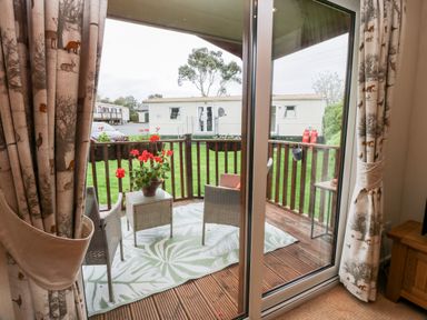 A balcony with chairs table and flower pot overlooking a grass area with mobile homes at Eden Lodge in Castlewigg near Whithorn