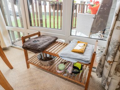 A wooden shelf with towels a metal bowl a tennis ball and dog leashes by a glass door at Eden Lodge Castlewigg near Whithorn