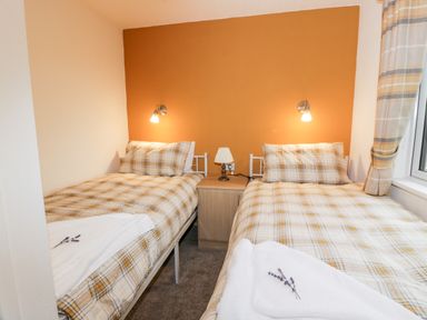A bedroom with two single beds and plaid bedding with a bedside table and lamps at Eden Lodge in Castlewigg near Whithorn