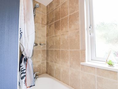 A bathroom with a bathtub shower curtain and a frosted window with a small plant on the sill at Eden Lodge in Castlewigg near Whithorn