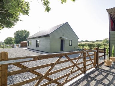A single story house with green siding behind a wooden gate on a gravel driveway at Southend in Welland