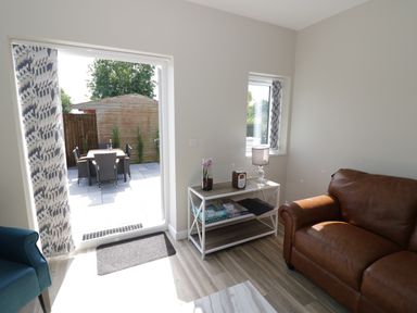 Living room with brown leather sofa blue chair white table with lamp and board games and patio door opening to outdoor dining area at Southend in Welland