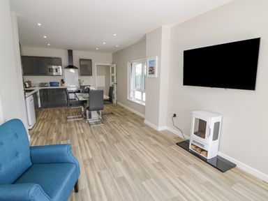 A room with kitchen and dining area including black chairs and a blue armchair and a wall mounted TV at Southend in Welland