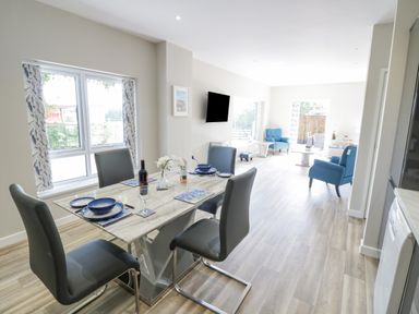 A dining area with a table set for four and a living room with blue chairs and a wall-mounted TV at Southend in Welland