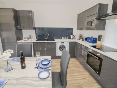 A modern kitchen with grey cabinets a washing machine oven microwave dining table with plates wine bottle and chairs at Southend in Welland
