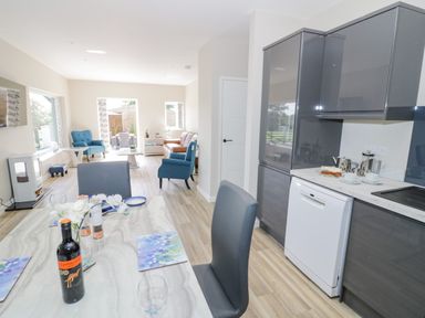 An open plan kitchen and living room with a dining table set with wine and plates and grey cabinets in the kitchen at Southend in Welland