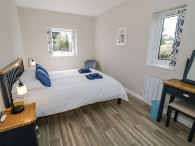 A bedroom with a double bed two windows a chair bedside table with lamp and a dressing table at Southend in Welland