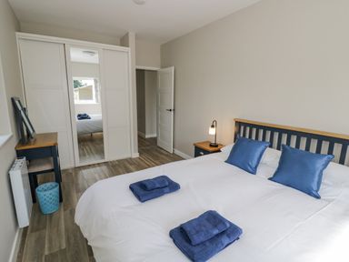 A bedroom with a double bed blue pillows and towels a bedside table with lamp a wardrobe with mirrored door and a desk with a chair at Southend in Welland