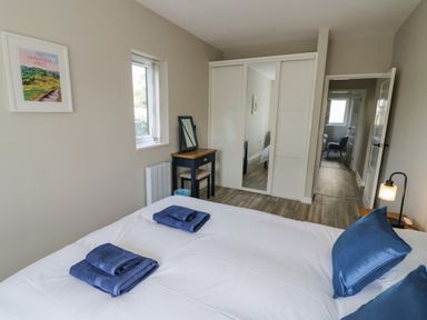 A bedroom with a bed with blue pillows and folded towels a desk with a mirror a window and a wardrobe with mirrored doors at Southend in Welland