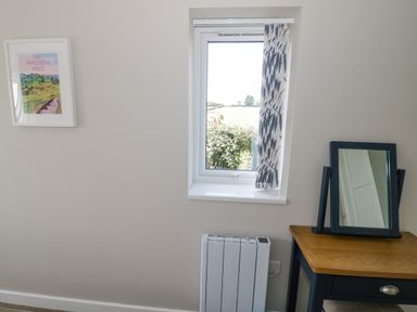 A room with a window and patterned curtain a framed picture a radiator and a wooden table with a mirror on top at Southend in Welland