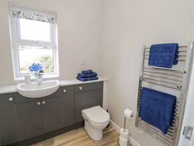 A bathroom with a sink, toilet, blue towels, and a window with a floral blind at Southend in Welland