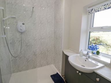 A bathroom with a shower area with a glass screen and a sink beneath a window with a floral curtain at Southend in Welland