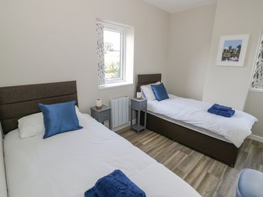 A bedroom with two single beds each with blue pillows and folded towels two bedside tables under a window at Southend in Welland