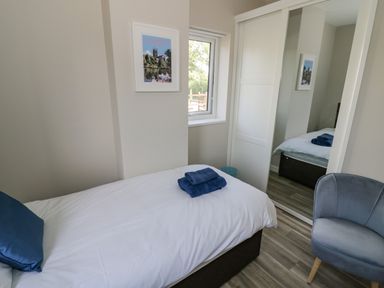 A bedroom with a single bed, blue pillows, folded towels, a window, a chair, and a wardrobe with mirrored sliding doors at Southend in Welland