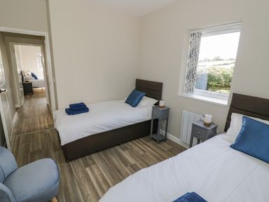A bedroom with two single beds blue pillows and towels wooden floor and a window at Southend in Welland