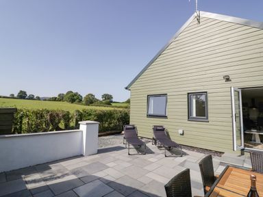 An outdoor patio with two lounge chairs and a table with chairs next to a house with green siding and two windows at Southend in Welland