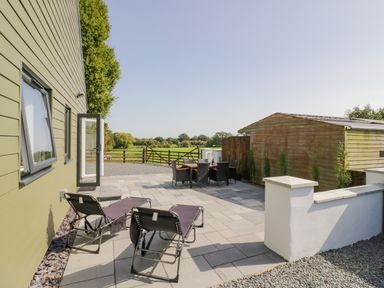 An outdoor patio area with two lounge chairs, a dining table with six chairs, a wooden shed, and a green wooden house at Southend in Welland