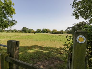 A green field with trees in the distance and a public footpath sign on a wooden post at Southend in Welland