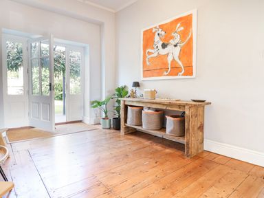 A wooden floor room with open double doors a wooden table with baskets plants and a painting at Charmouth Lodge in Charmouth
