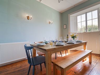 A dining room with a wooden table set for a meal next to a window with half shutters at Charmouth Lodge in Charmouth
