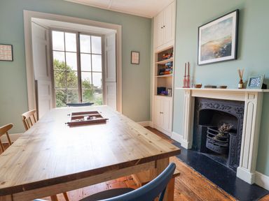 A dining room with a wooden table and chairs a window fireplace and shelves with board games at Charmouth Lodge in Charmouth