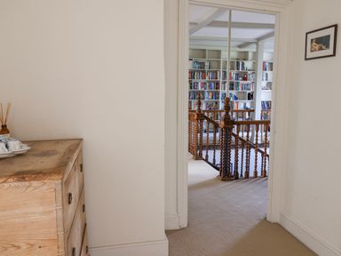 A corridor with a wooden chest of drawers leading to a room with bookshelves and a wooden staircase at Charmouth Lodge in Charmouth